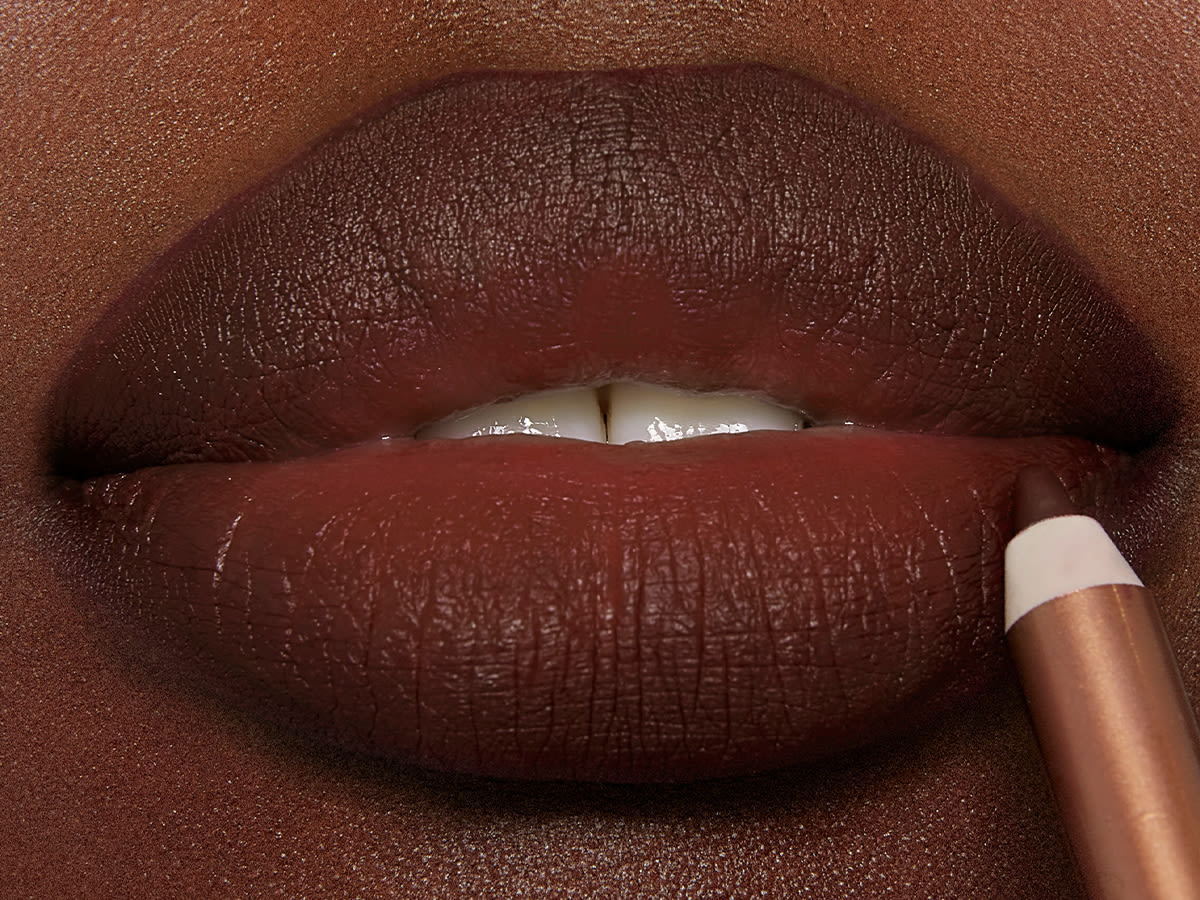 Lip cheat lip liner in Pillow Talk Intense on deep-tone model lips close-up Lips close-up of a deep-tone model applying a lush, tawny brown lip liner pencil.