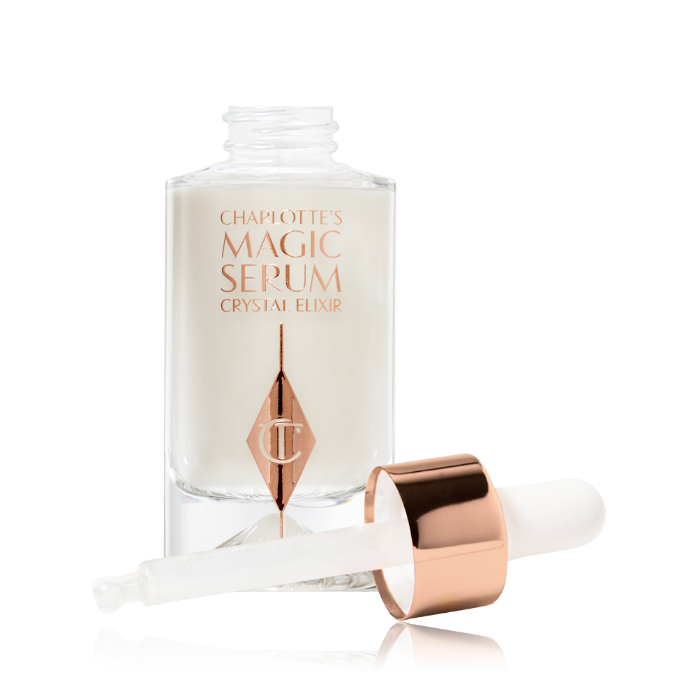Charlotte's Magic Serum Crystal Elixir Open A pearly-white serum in a glass bottle with its dropper applicator next to it.