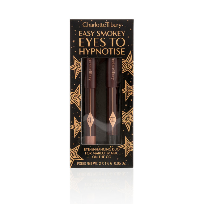 Two chubby eyeshadow sticks, in coppery-brown and black, inside their packaging that has the text, 'Easy smokey eyes to hypnotise' written on it along with shiny gold stars printed all over.