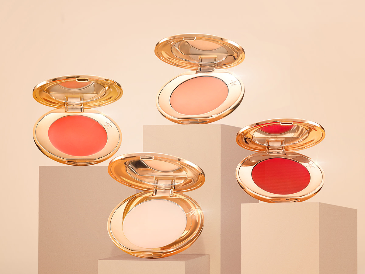 A collection of four colour corrector compacts with mirrored lids in light peach, medium-peach, orange, and burnt orange colours. 