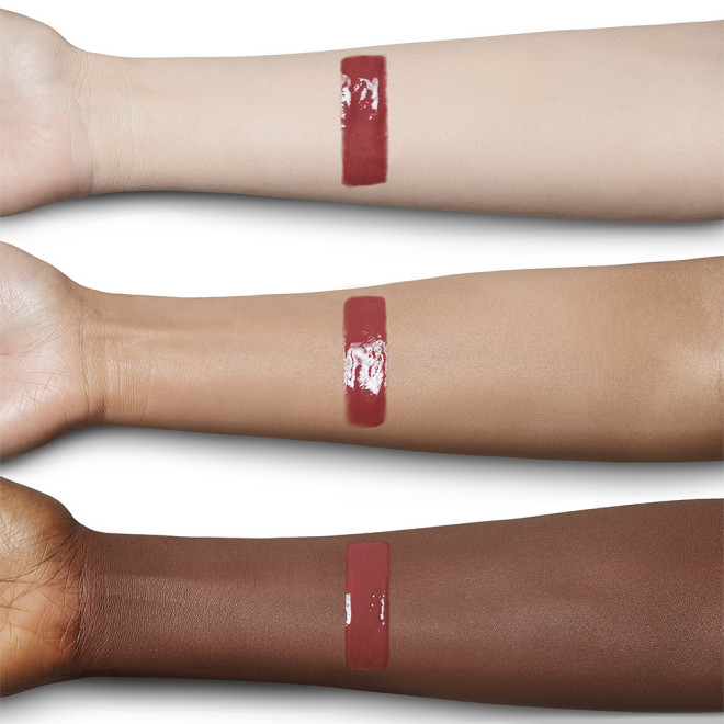 Swatch of a lip gloss in a berry-pink shade on fair, tan, and deep-tone arms.