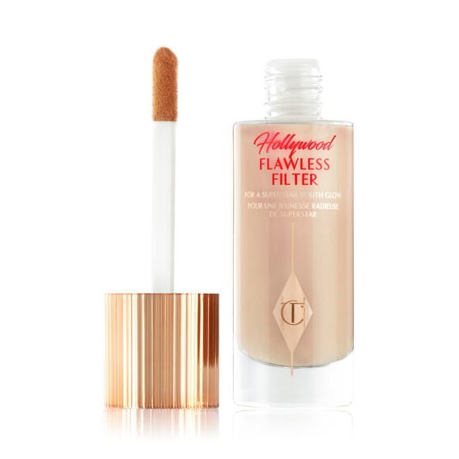 An open, luminous primer in a light cool-toned-beige shade in a glass bottle with its gold and white doe-foot applicator next to it.