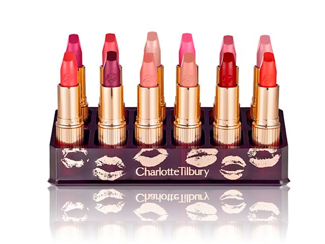 Hot Lips Lipstick Wardrobe open A collection of matte lipsticks in shades of red, pink, peach, and purple with golden-coloured packaging, inside a purple-coloured lipstick holder with kiss prints all over it.