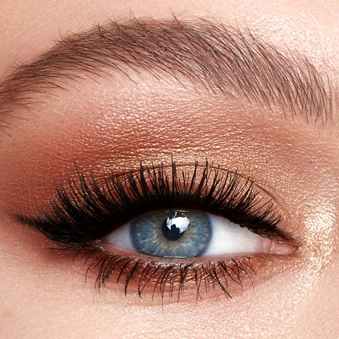 Single-eye close-up of a fair-tone model with blue eyes wearing metallic honey gold, soft amber, and dark chocolate brown eye makeup. 