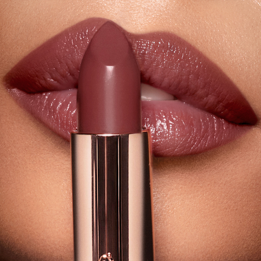K.I.S.S.I.N.G Pillow Talk Intense Lipstick olive skin model A deep, berry-pink lipstick in a metallic, golden tube held up in front of an olive skin model wearing the same shade.