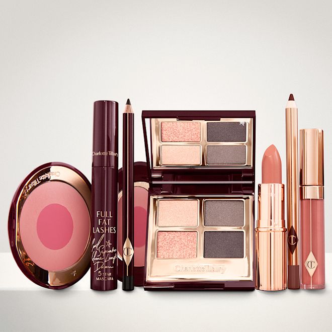 The Uptown Girl Deep Look kit displayed An open two-tone blush in cool-toned pink and fuchsia with a mascara, eyeliner pencil, quad eyeshadow palette with shimmery and matte grey and golden shades, an open lipstick in nude red, lip liner pencil in taupe-brown, and a lip gloss in warm brown-peach.