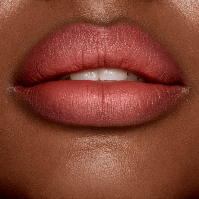 Lips close-up of a deep-tone model wearing a matte, golden peachy-pink lipstick.