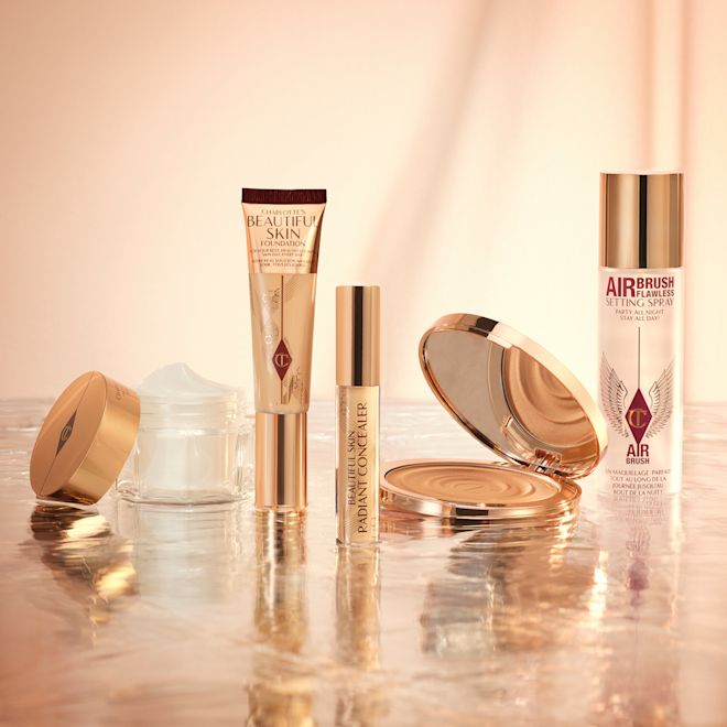 5 Steps To Beautiful Skin kit displayed Foundation in a sleek gold-coloured tube with a concealer in a glass tube and gold-coloured lid, dark brown cream bronzer compact in gold-coloured packaging, setting spray in a large, clear bottle with a gold-coloured lid, and pearly-white face cream in a glass jar with a gold-coloured lid.
