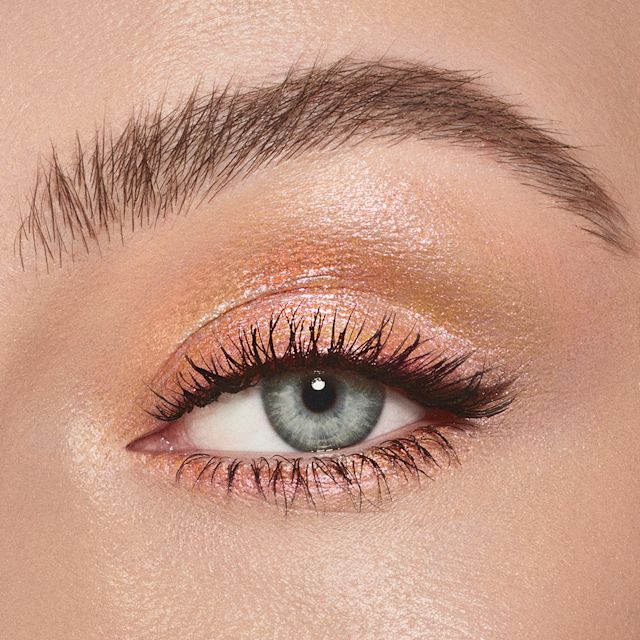 Eyes to Mesmerise in Sunlit Glow on blue eyes close-up Single-eye close-up of a fair-tone model with blue eyes applying a golden pink duo-chrome-effect cream eyeshadow with a duo-chrome metallic finish,