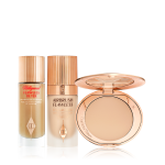 Glowy primer in a glass bottle with a gold-coloured-lid, foundation in a frosted glass bottle with a gold-coloured lid, and pressed powder compact with a mirrored-lid in a light shade.