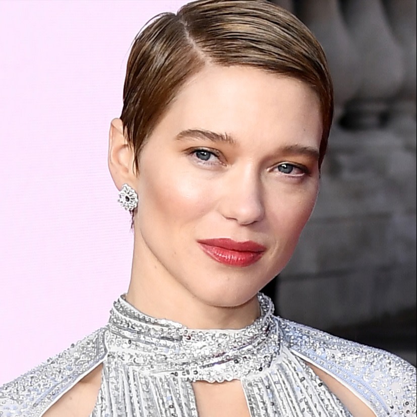 Léa Seydoux wearing soft, barely-there eye makeup with a glowy pink blush and subtle highlighter with bold, red lipstick and a shiny, silver-coloured dress. 