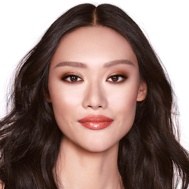 The Glowing Goddess look on fair-tone model with brown eyes A fair-tone brunette model with brown eyes wearing shimmery brown eye makeup with orange-red lip gloss, bronzed cheeks, and glowy nude pink blush.