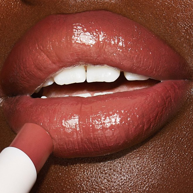 Lips close-up of a deep-tone model applying a moisturising lipstick lip balm in a dreamy peach rose shade.