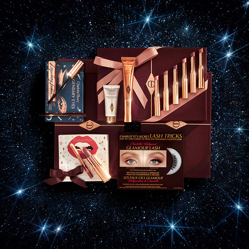 A collection of different makeup products that include lip kits, eye shadow palettes, lipsticks, highlighters and primers, and eye kits, all in front of a starry background. 