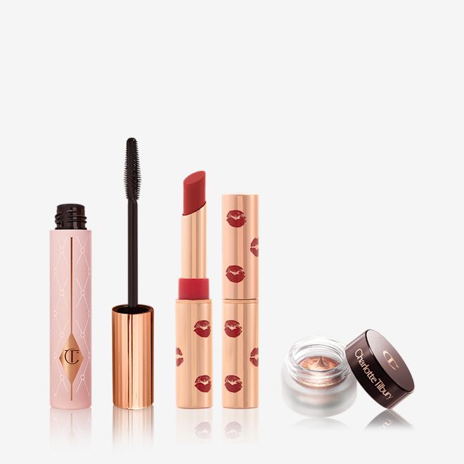 Party Eye and Lip Kit open Black mascara in a sheer pink tube with a gold-coloured lid and fluffy applicator, open matte lipstick in a poppy-red colour with kiss prints printed all over the golden-coloured lipstick tube, and cream eyeshadow in an antique oyster-gold shade. in a petite pot with its lid next to it.