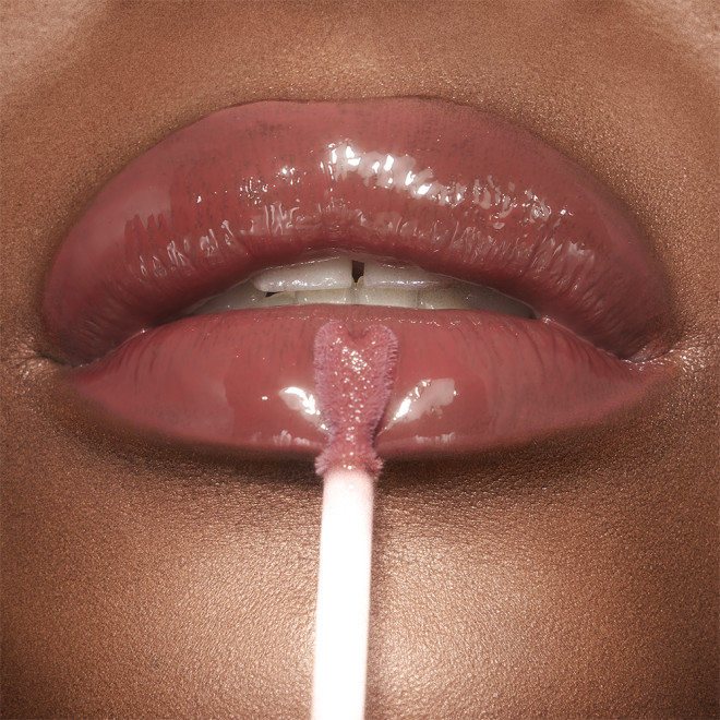 A deep-tone model applying a berry-pink lip gloss on her lips with a heart-shaped applicator. 