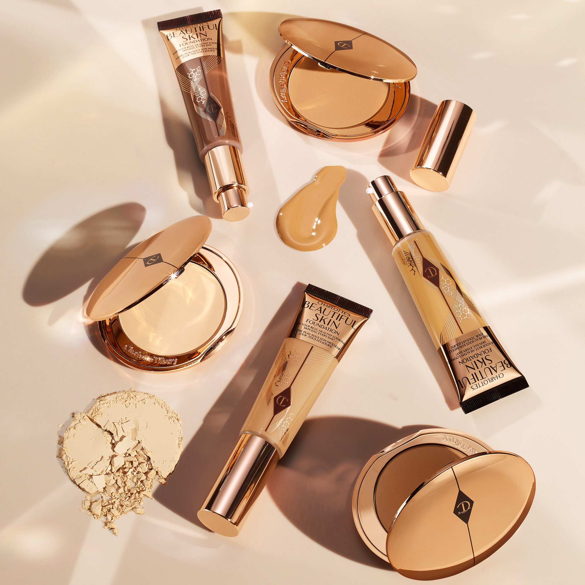 A collection of open, foundation tubes in gold packaging with a collection of open powder compacts in gold-coloured packaging. 