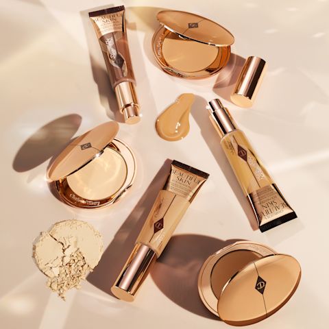 A collection of open, foundation tubes in gold packaging with a collection of open powder compacts in gold-coloured packaging.