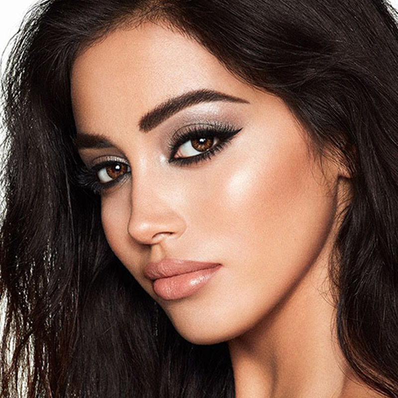 Model with brown eyes wearing a smokey silvery eyeshadow look with bronzed cheeks and glossy nude-peach lips.