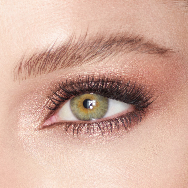 Single-eye close-up of a light tone model with green eyes wearing cream eyeshadow in an antique oyster-gold shade.