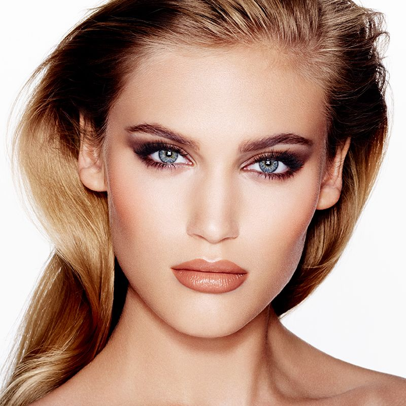 A fair-tone model with blue eyes wearing glowy peach makeup with smokey eyeshadow that makes her eyes look bigger. 