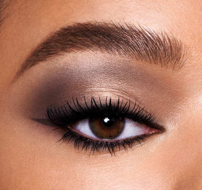 Single-eye close-up of a medium-tone model with brown eyes wearing a smokey grey, light brown, and gold eye look with black wing eyeliner.