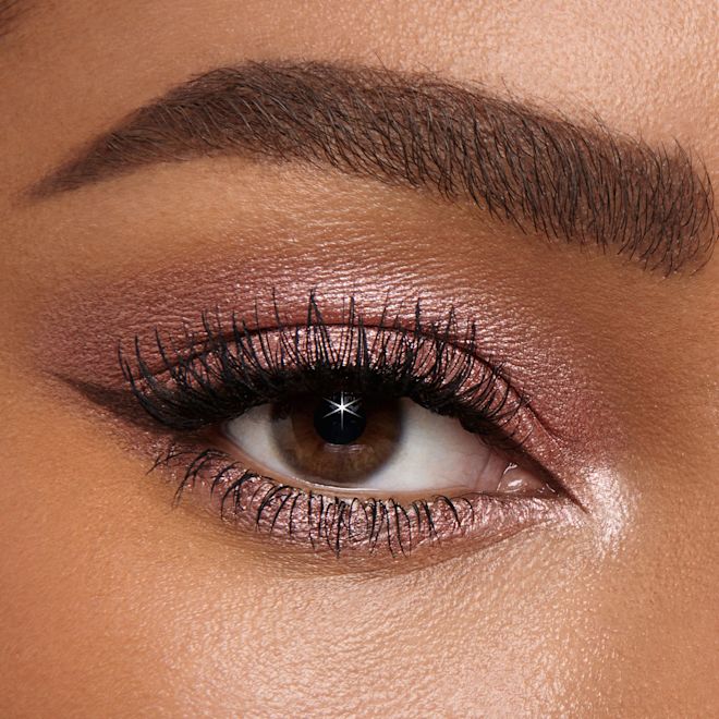 Colour Chameleon in Pillow Talk on brown eye close-up Single-eye close-up of a deep-tone model with brown eyes wearing shimmery rose gold eyeshadow with black eyeliner.