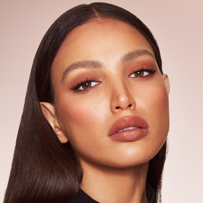 Medium-tone brunette model with brown eyes wearing nude brown matte eye makeup with nude pink lip and cheek cream as blush and lipstick, and glowy opal-coloured highlighter.