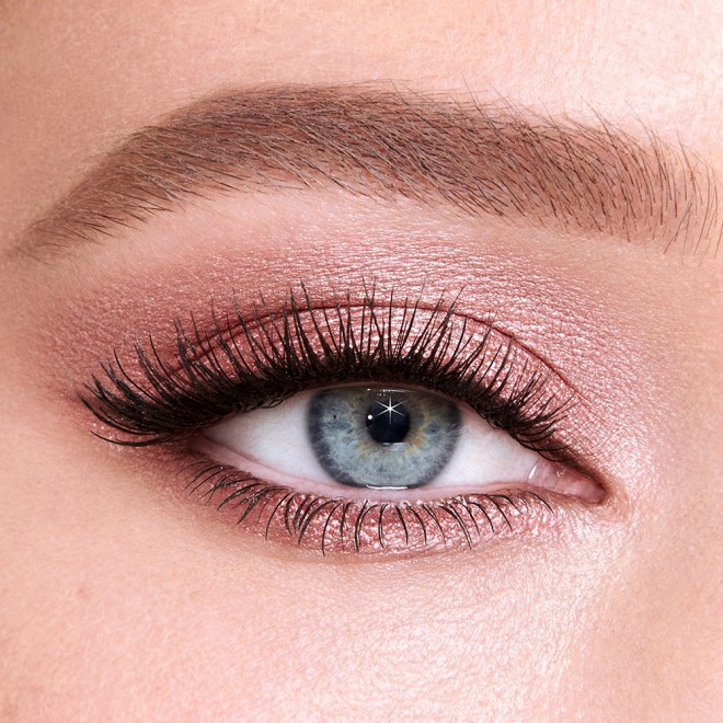 Single-eye close-up of a fair-tone model with blue eyes wearing shimmery nude pink eye makeup and berry-brown eyeliner. 