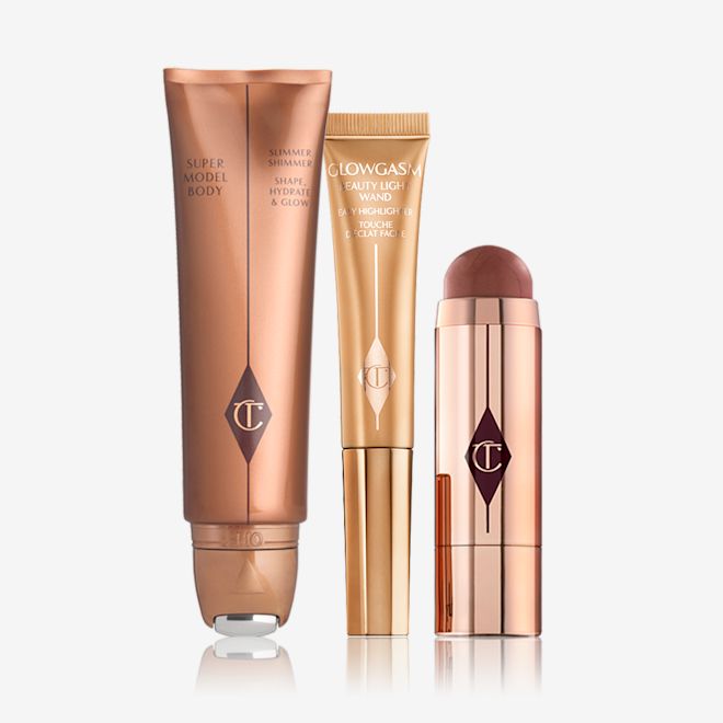 Sun-kissed Glowing Goddess Kit displayed Body highlighter wand in a bronze tube, face highlighter wand in a honey-gold tube, a blush stick in a berry-red shade in gold packaging.