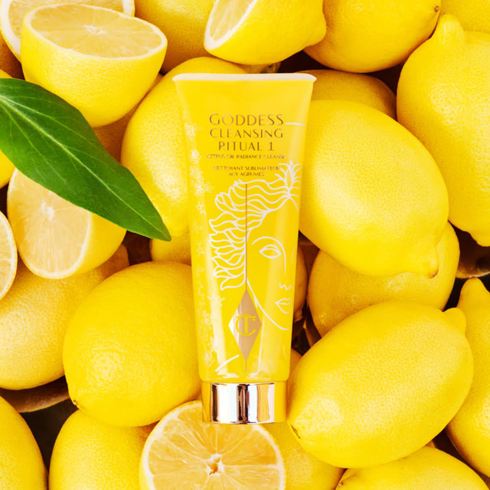 A lemon-yellow cleanser with a white-gold coloured lid on top of a bed of lemons. 