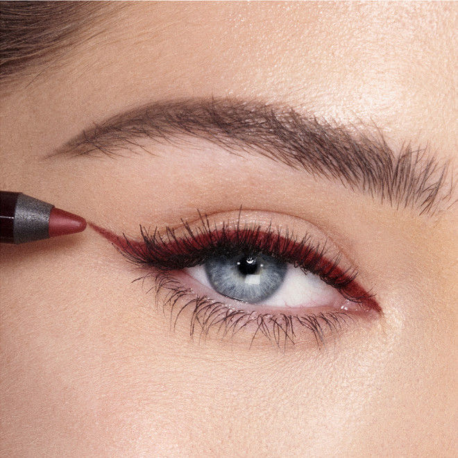 Close-up of a fair-tone model with blue eyes applying a berry-pink eyeliner in a sharp wing style.