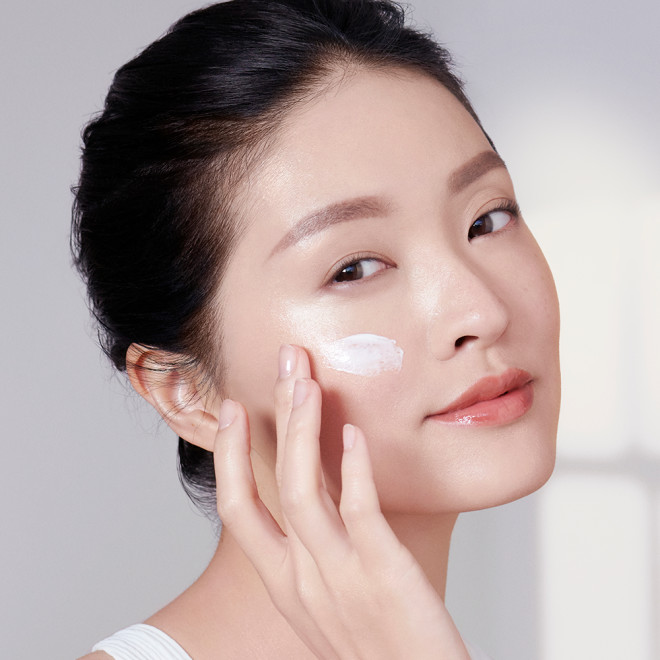 A fair-tone brunette model applying a pearly-white face cream on her cheek. 