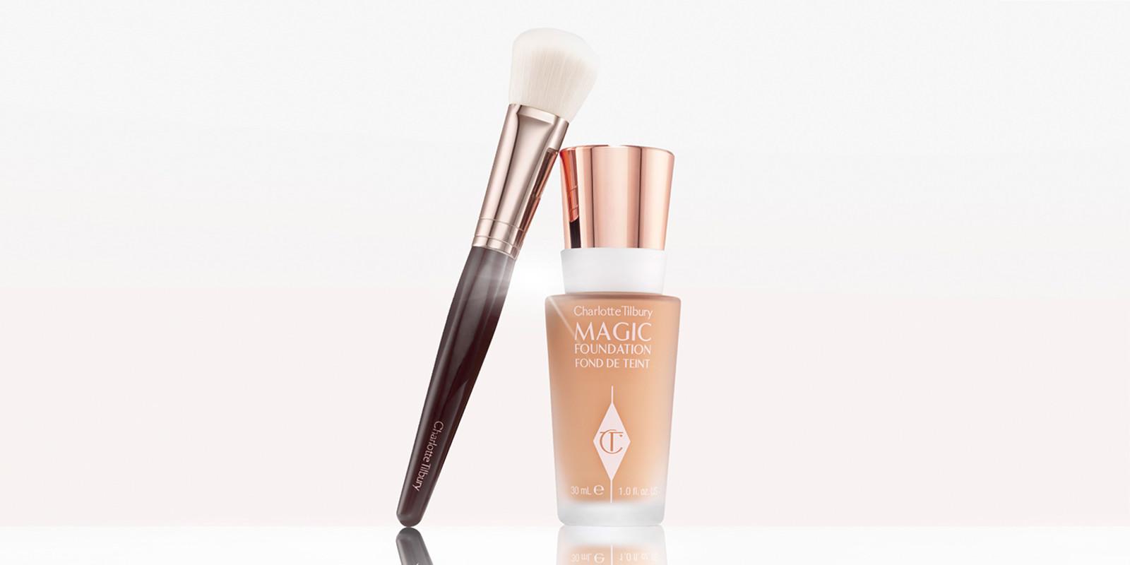 Foundation in a glass bottle with the CT logo embossed on it with a rose-gold, metallic lid placed next to a foundation brush. 