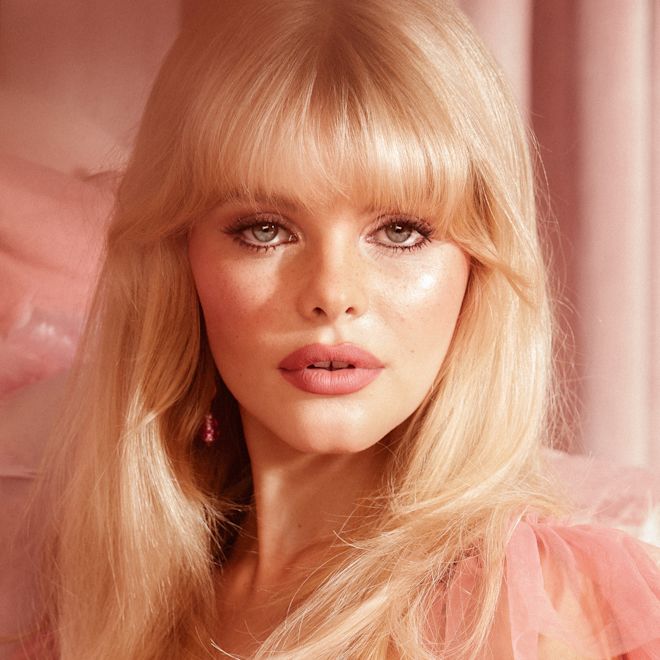 Beauty Light Wand in Pillow Talk on fair-tone model fair-tone blonde model wearing nude pink matte lipstick, and smokey brown eye makeup with a light pink liquid highlighter-blush.