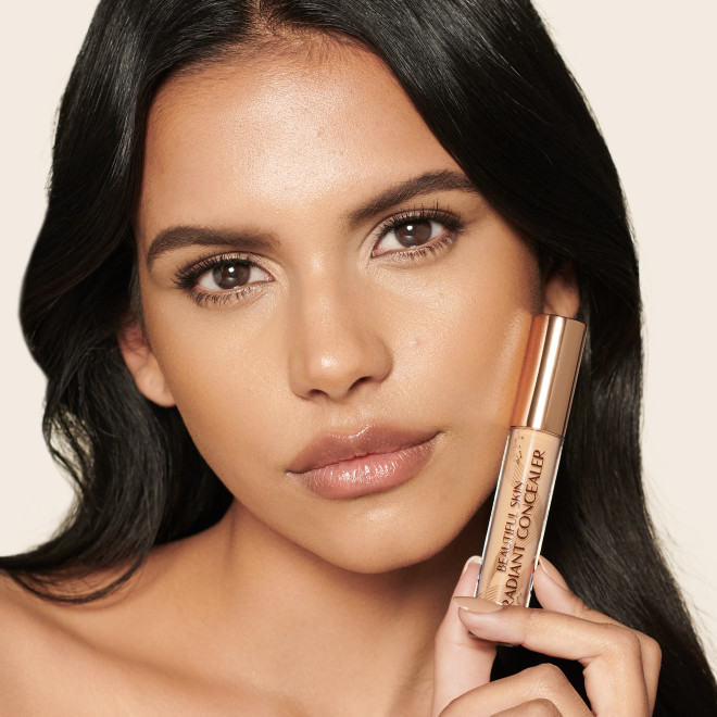 Medium-tone model with brown eyes wearing a radiant, concealer that brightens, covers blemishes, and makes her skin look fresh along with nude lip gloss and subtle eye makeup.