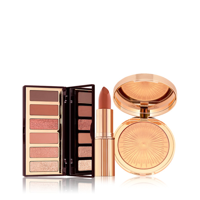 An open, 6-pan eyeshadow palette with a mirrored lid and matte and shimmery eyeshadows in shades of pink, pink, and brown, an open lipstick in a nude brick rose shade, and a highlighter compact in a soft gold shade.