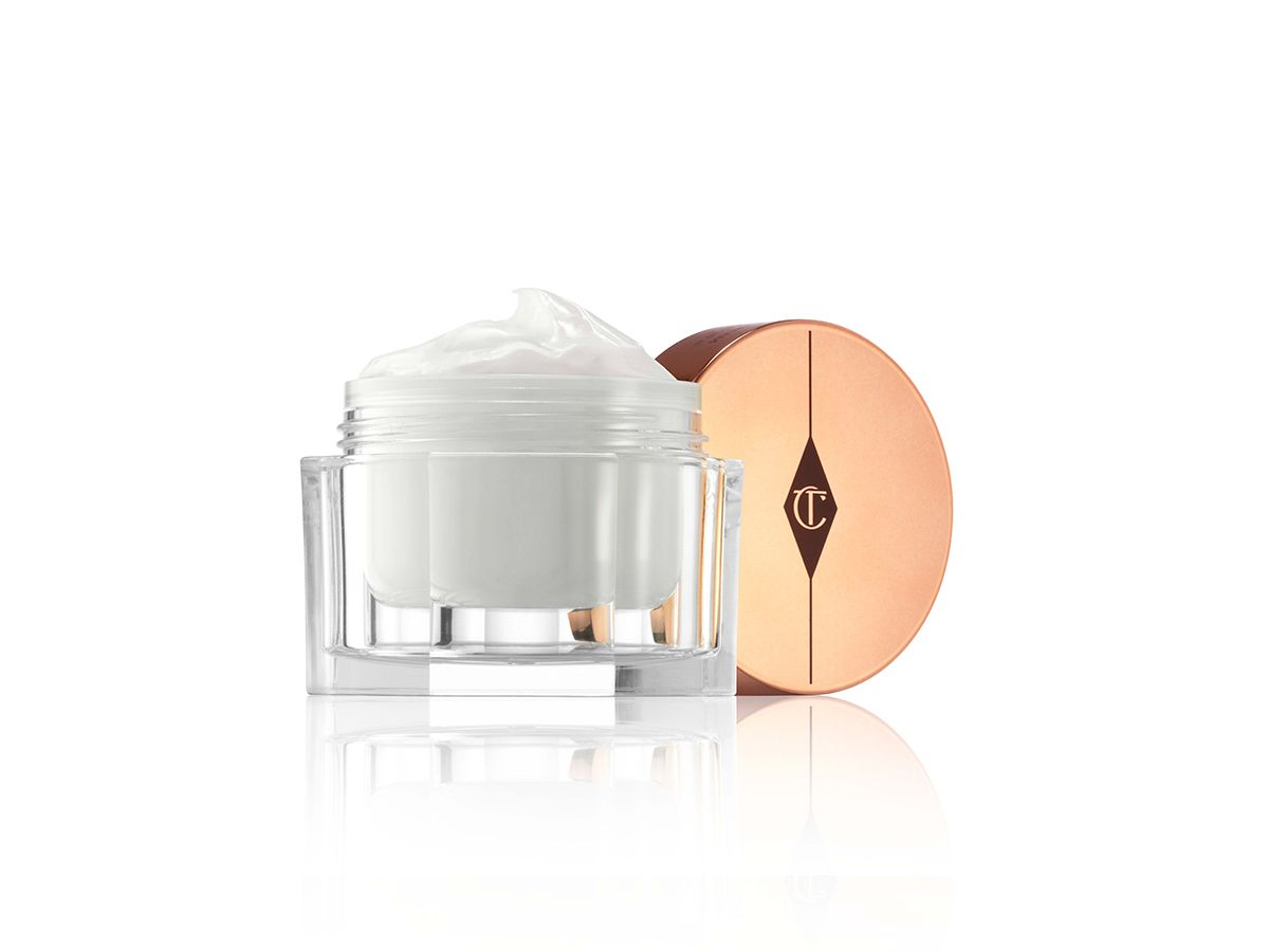 Magic Cream lid removed Thick and luscious pearly-white moisturiser in an open glass jar with its gold-coloured lid placed behind it.