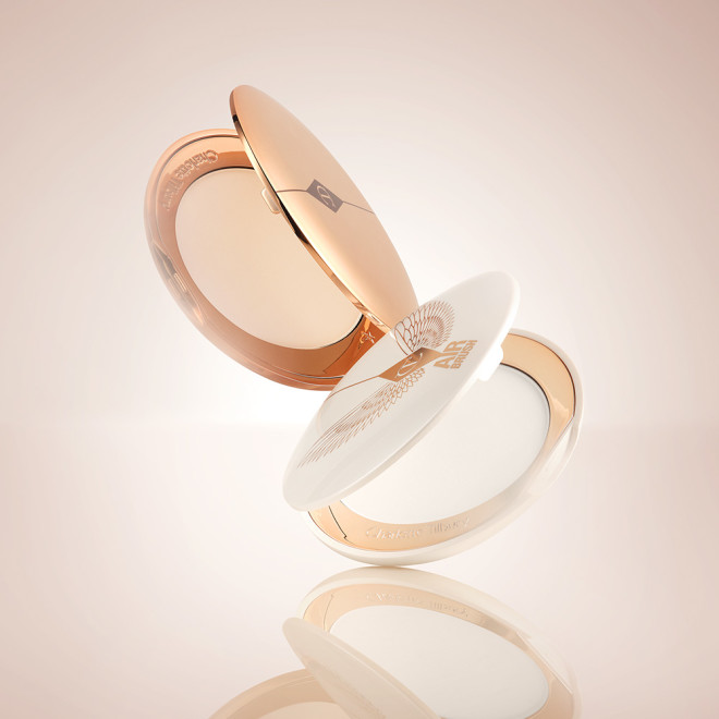 Two, open, setting powder compacts with mirrored-lids and white and gold-coloured packaging.