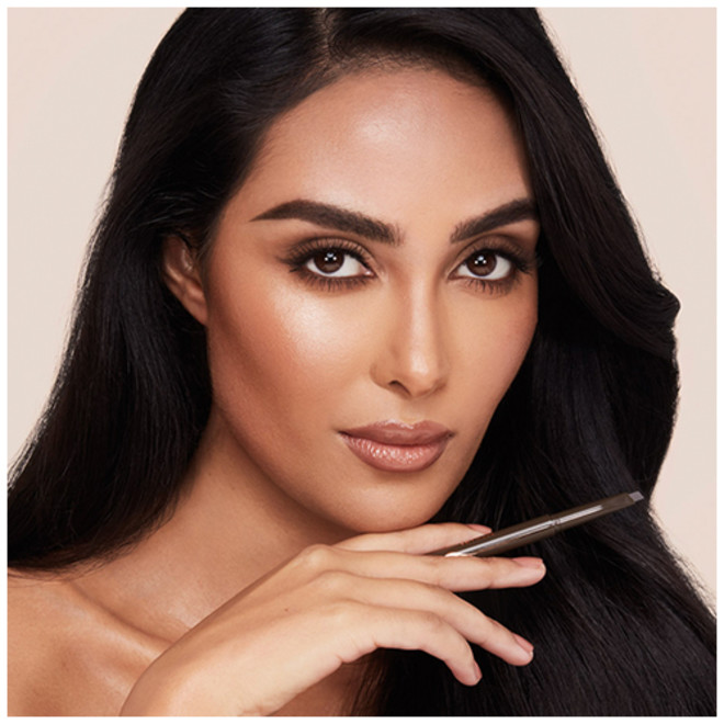 A medium-tone brunette model with brown eyes wearing nude matte lipstick with smokey eye makeup and her thick, lush brows shaped, lined, and filled in a black-brown colour.