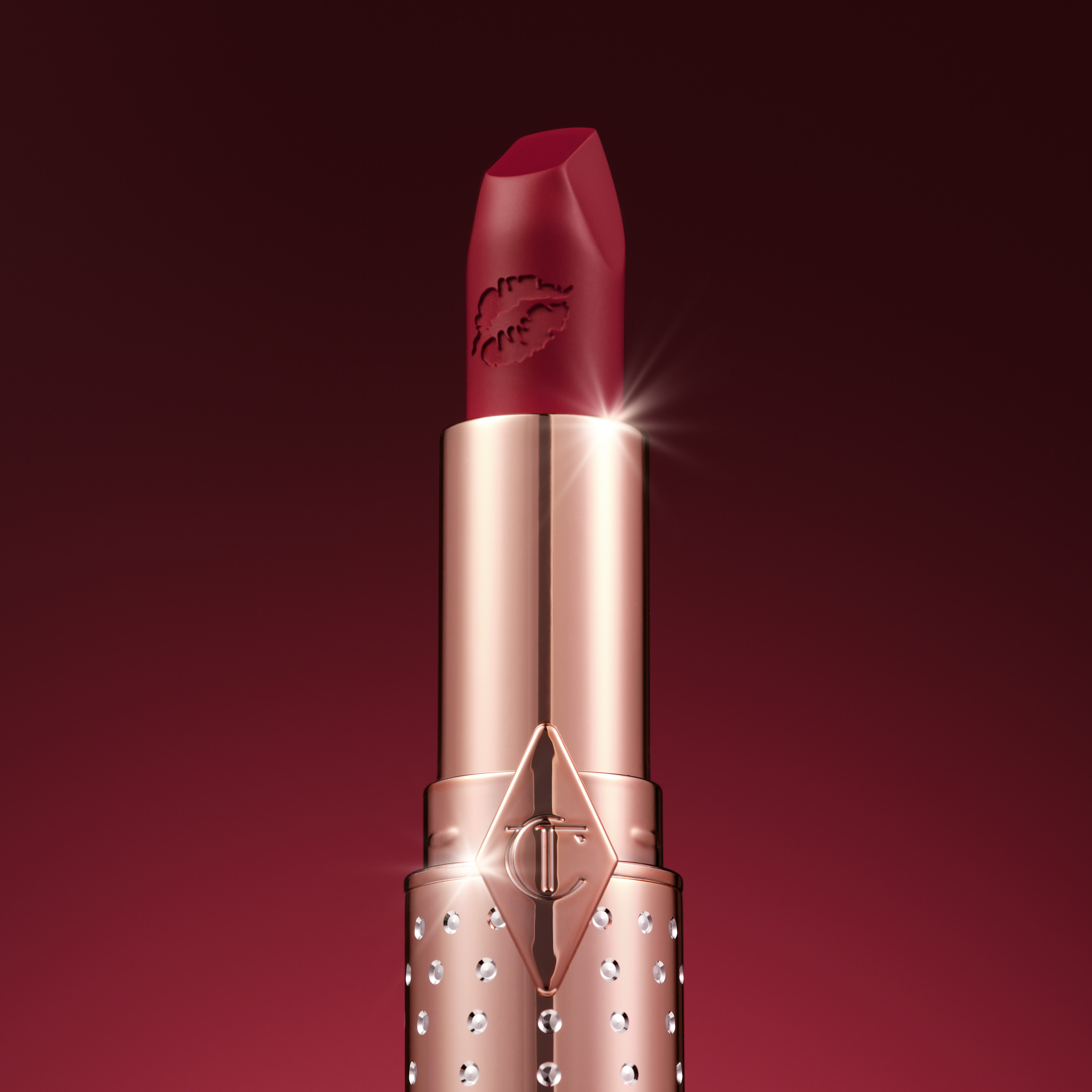 Deep crimson red lipstick called Coronation Red with lid off and bejewelled packaging
