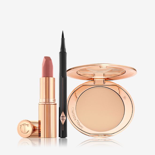Airbrush Complexion Feline Flick Pillow Talk Kit An open nude-pink lipstick in a golden tube with an open black eyeliner pen, and open, mirrored-lid pressed compact in a light shade.
