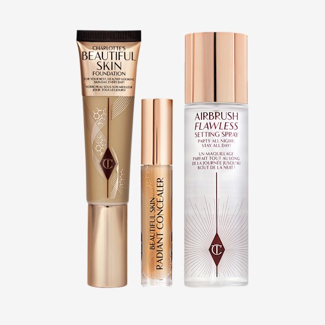 Beautiful Skin, Conceal, Perfect, Set Kit Foundation in a sleek gold-coloured tube with a concealer in a glass tube and gold-coloured lid, dark brown cream bronzer compact in gold-coloured packaging, and setting spray in a large, clear bottle with a gold-coloured lid.