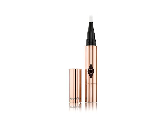 The Retoucher Concealer open An open concealer with a twist-up end, in rose-gold, metallic packaging with its lid next to it.