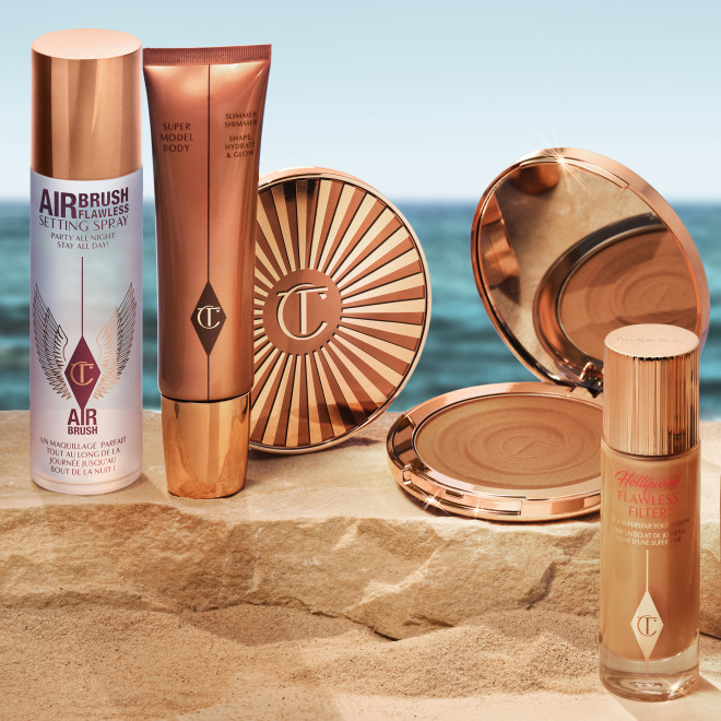 Setting spray in a clear bottle with a gold-coloured lid, body bronzing highlighter in a large golden-coloured tube with a gold-coloured lid, bronzer compact with a mirrored-lid, and dewy tinted primer in a frosted glass bottle with a gold-coloured lid.