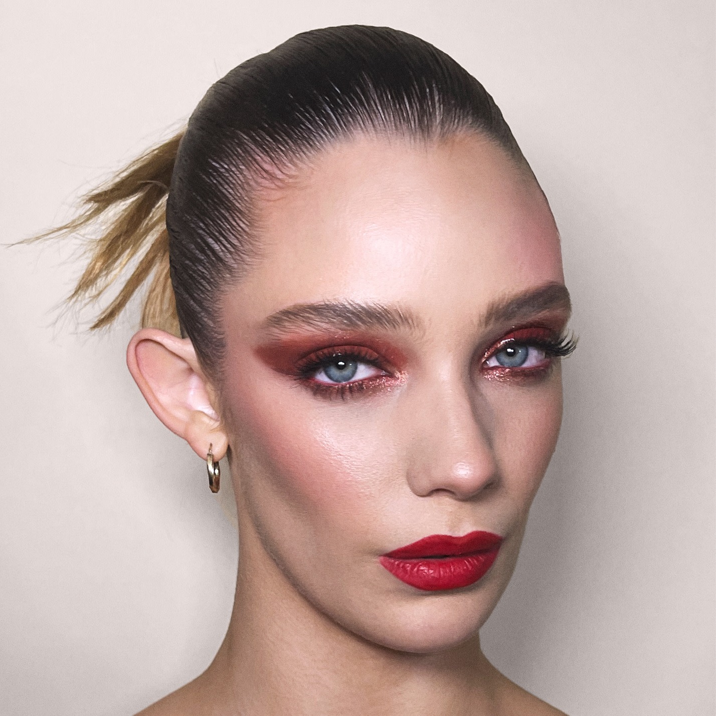 Close-up of a fair-tone model with blue eyes wearing bold red matte lipstick with berry rose and brown dramatic eye makeup with berry rose blush.