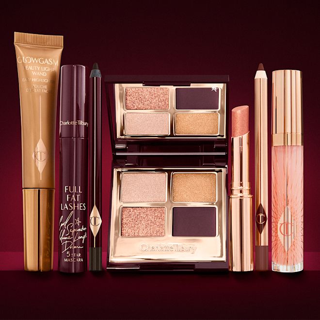The Queen of Glow Deep Look kit displayed A highlighter wand in a honey-gold-coloured tube with a mascara, eyeliner pencil, quad eyeshadow palette with shimmery and matte rose gold, plum, and golden shades, an open lipstick in nude coral, lip liner pencil in vampy red, and a lip gloss in nude pink.