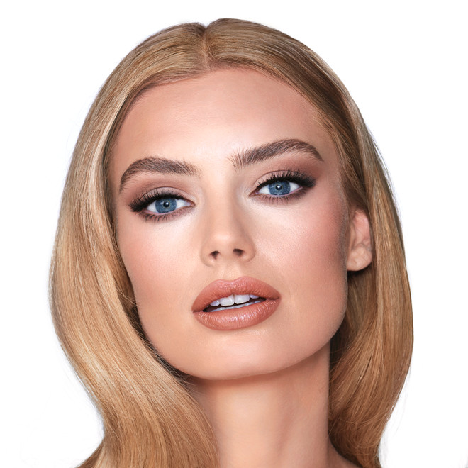 A light-tone model with blue eyes wearing smokey brown eye makeup with muted pink blush and glossy terracotta-brown lips.