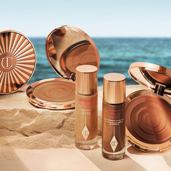 Hollywood Flawless Filter and Beautiful Skin Bronzer banner Collection of glowy primers in frosted glass bottles with gold-coloured lids and cream bronzer compacts in gold-coloured packaging with mirrored lids.