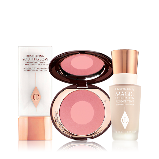 Charlotte's Magic Blush and Glow Complexion Kit displayed A primer in a white-coloured bottle with gold-coloured lid, an open two-tone blush in muted pink and pearlescent pink, and foundation in a glass bottle with a gold-coloured lid.